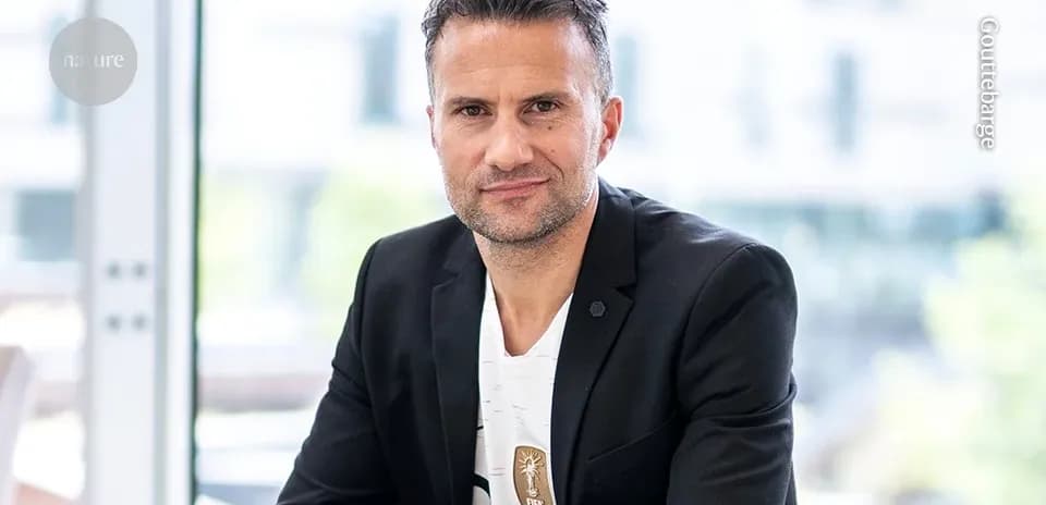 Man in suit posing indoors with a FIFA badge