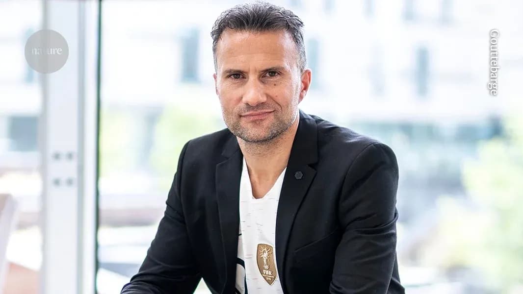 Man in suit posing indoors with a FIFA badge