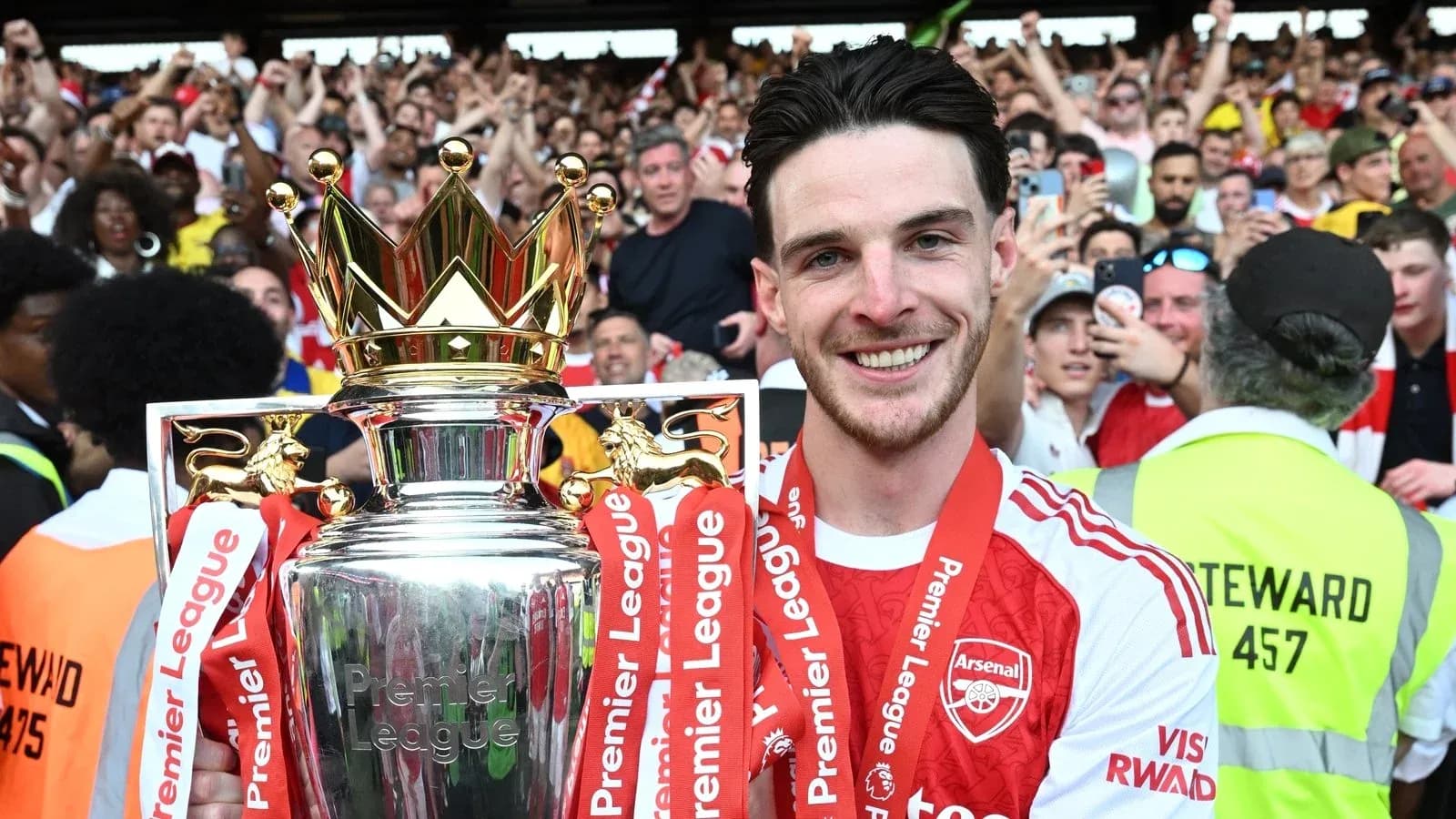 Player holding Premier League trophy with fans celebrating