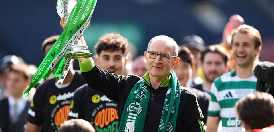 Manager holding trophy with celebrating players behind