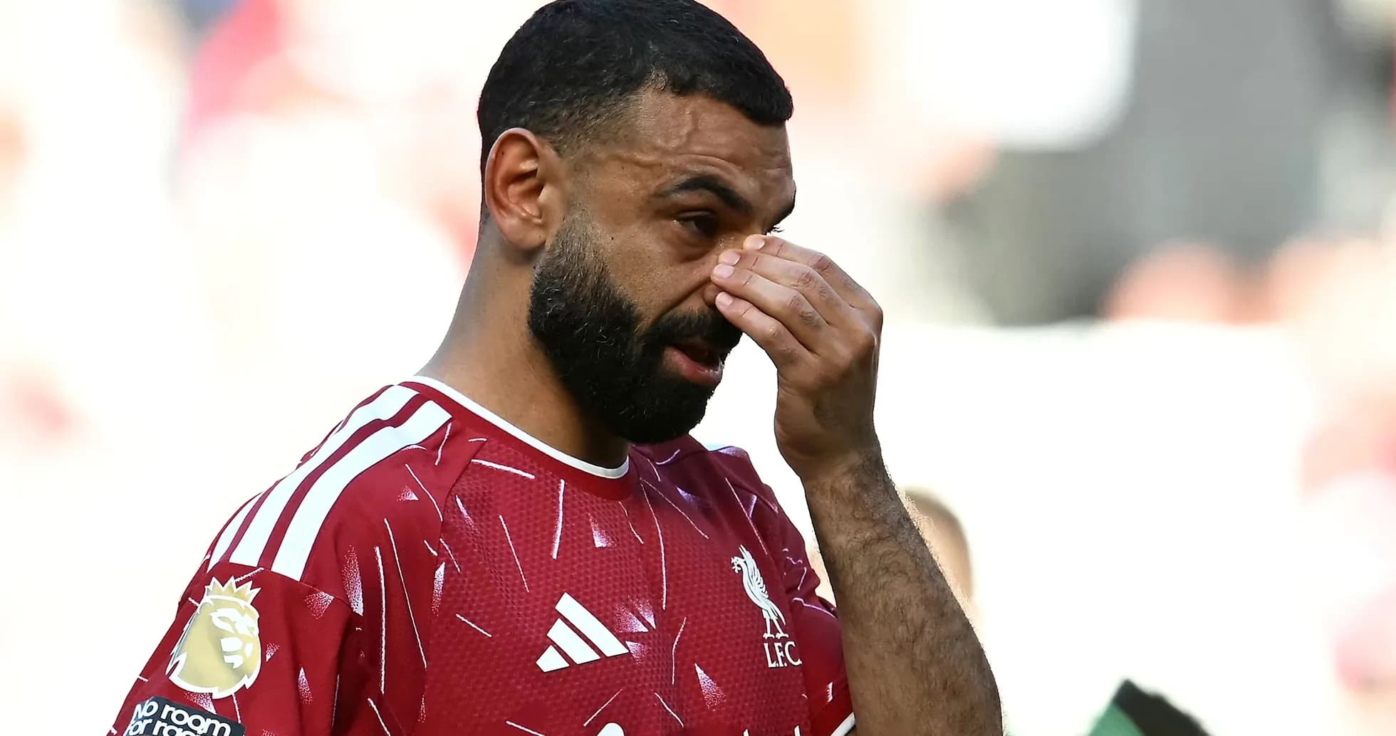 Player in Liverpool kit touching his face on pitch