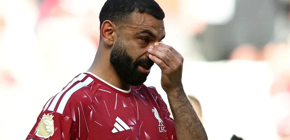Player in Liverpool kit touching his face on pitch