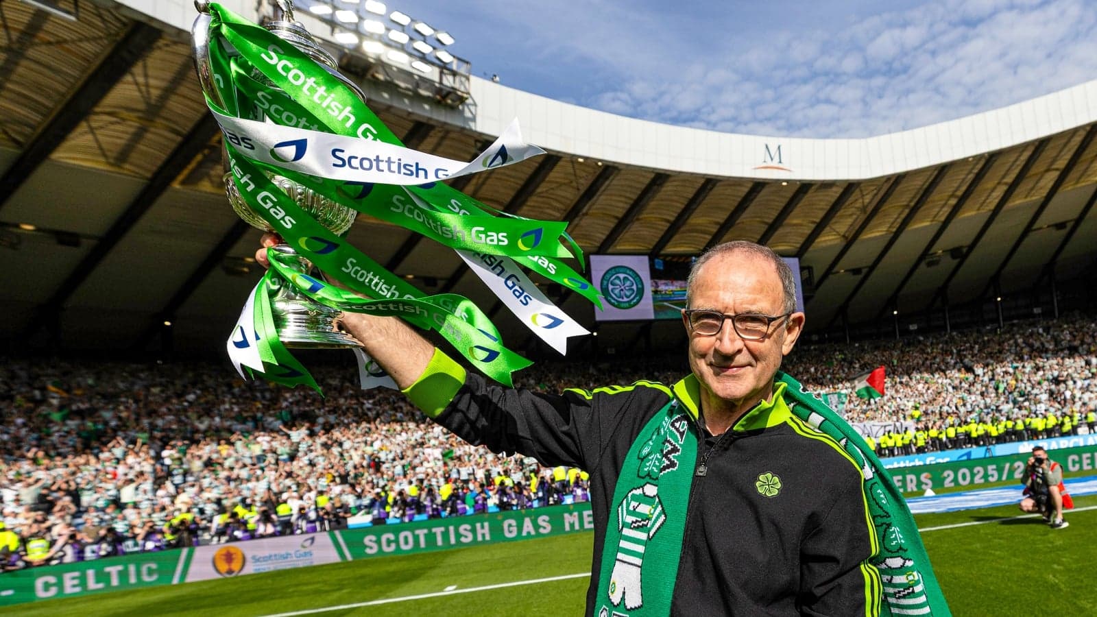 Man holding trophy with green ribbons at stadium
