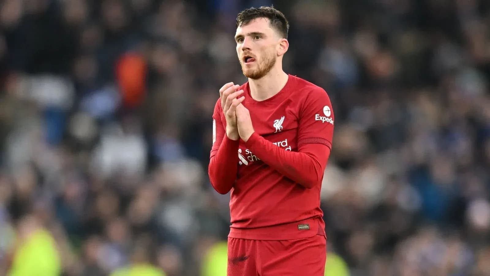 Player in red jersey applauding fans at stadium